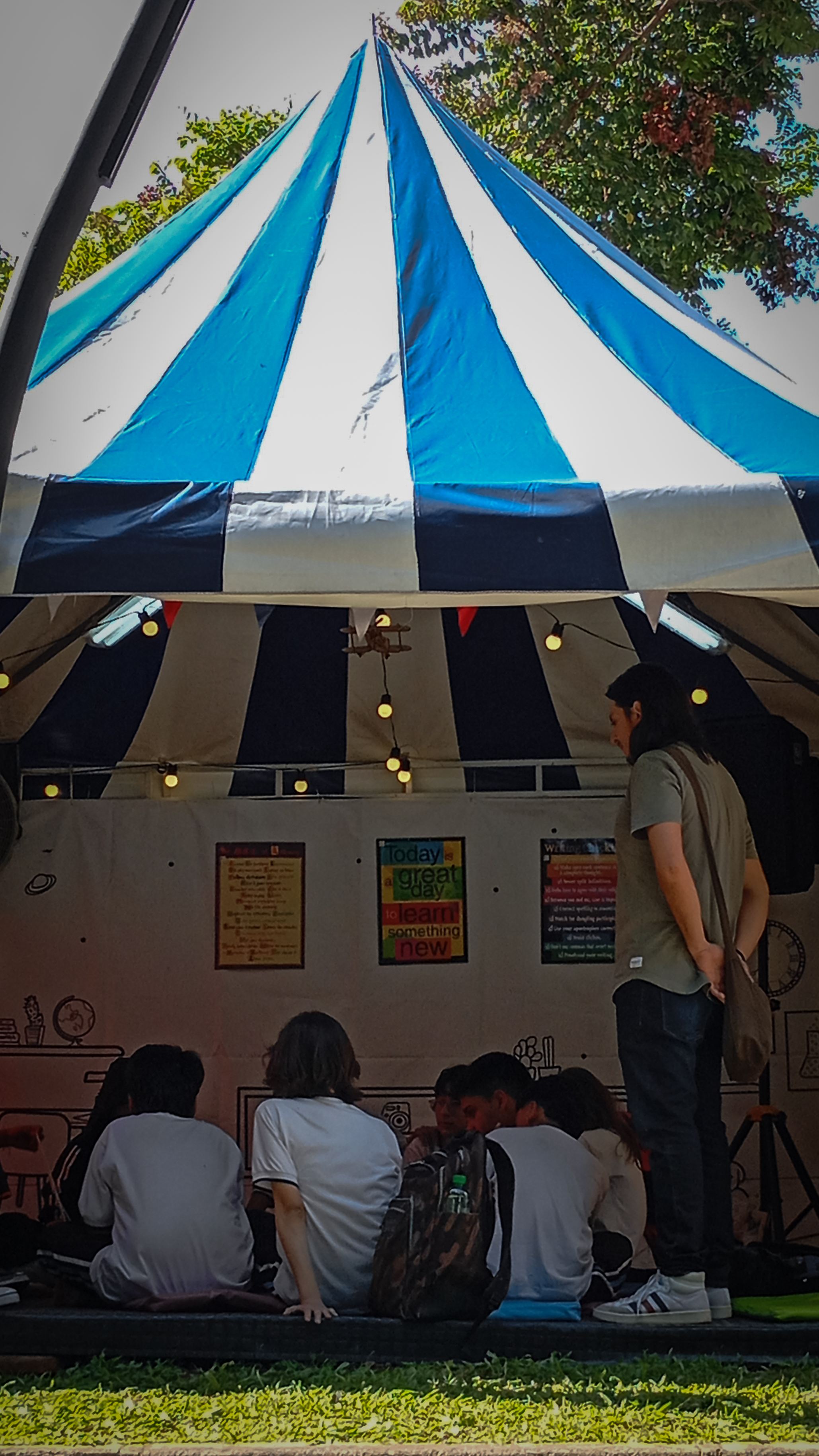 Estudiantes sentados y profesor de pie dentro de una carpa participando de un taller