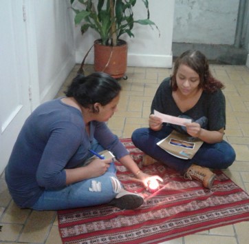 dos mujeres sentadas en el suelo, leyendo con vela encendida.