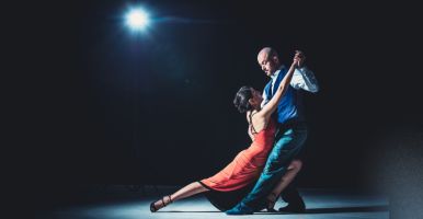 Un hombre y una mujer bailando tango en un escenario iluminado con armonía para apreciar la elegancia de sus pasos.