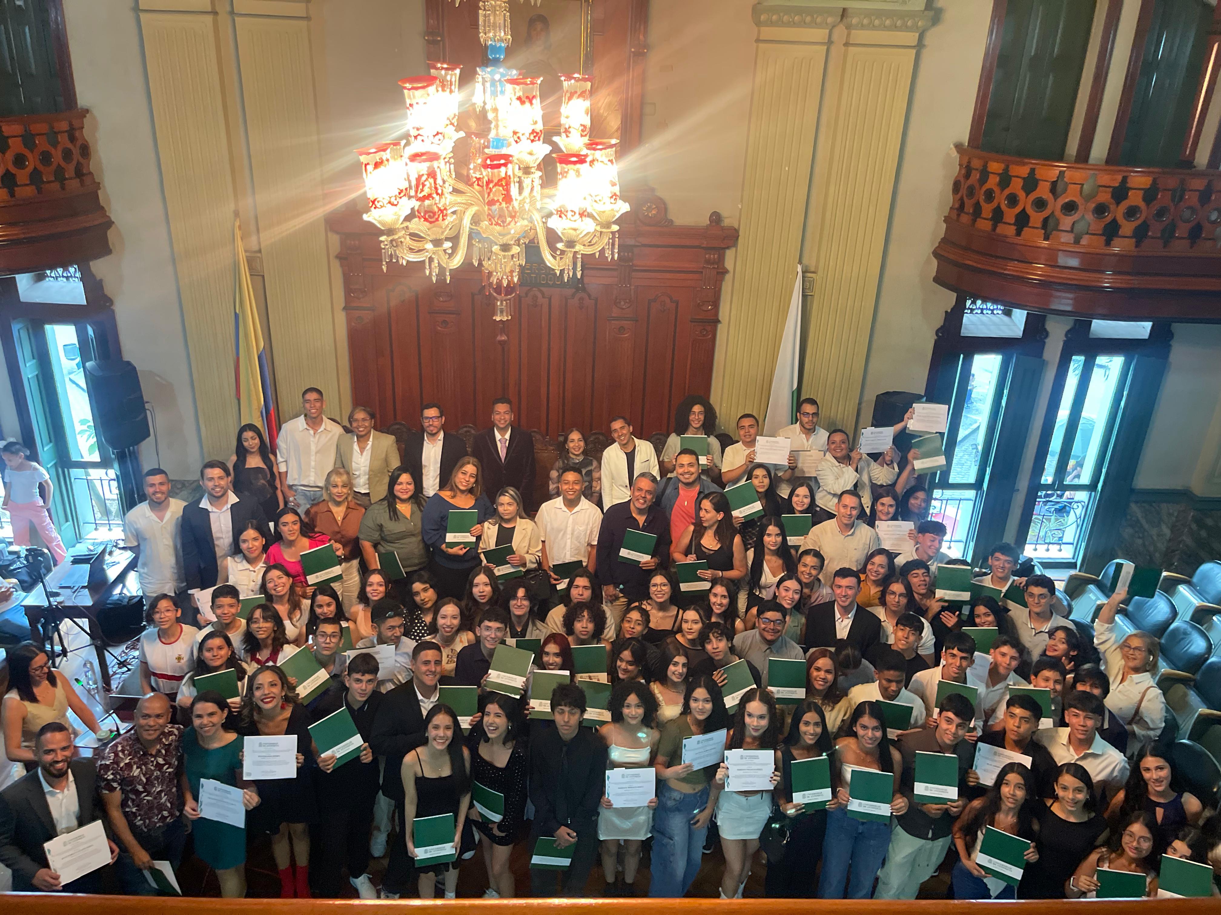 Foto tomada desde un balcón. Muchas personas de pie con diplomas en la manos