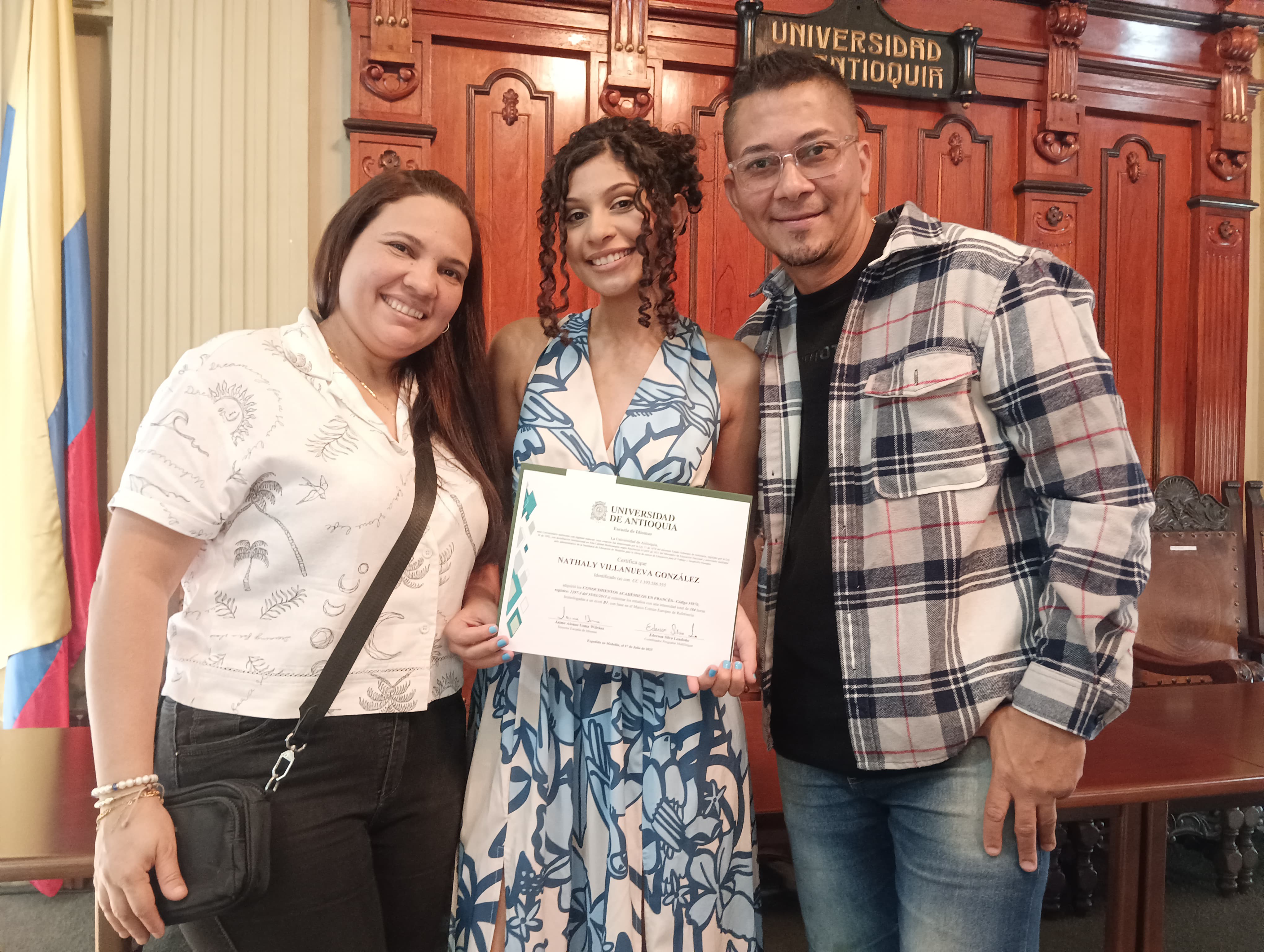 Tres personas de pie. La del medio con diploma en las manos