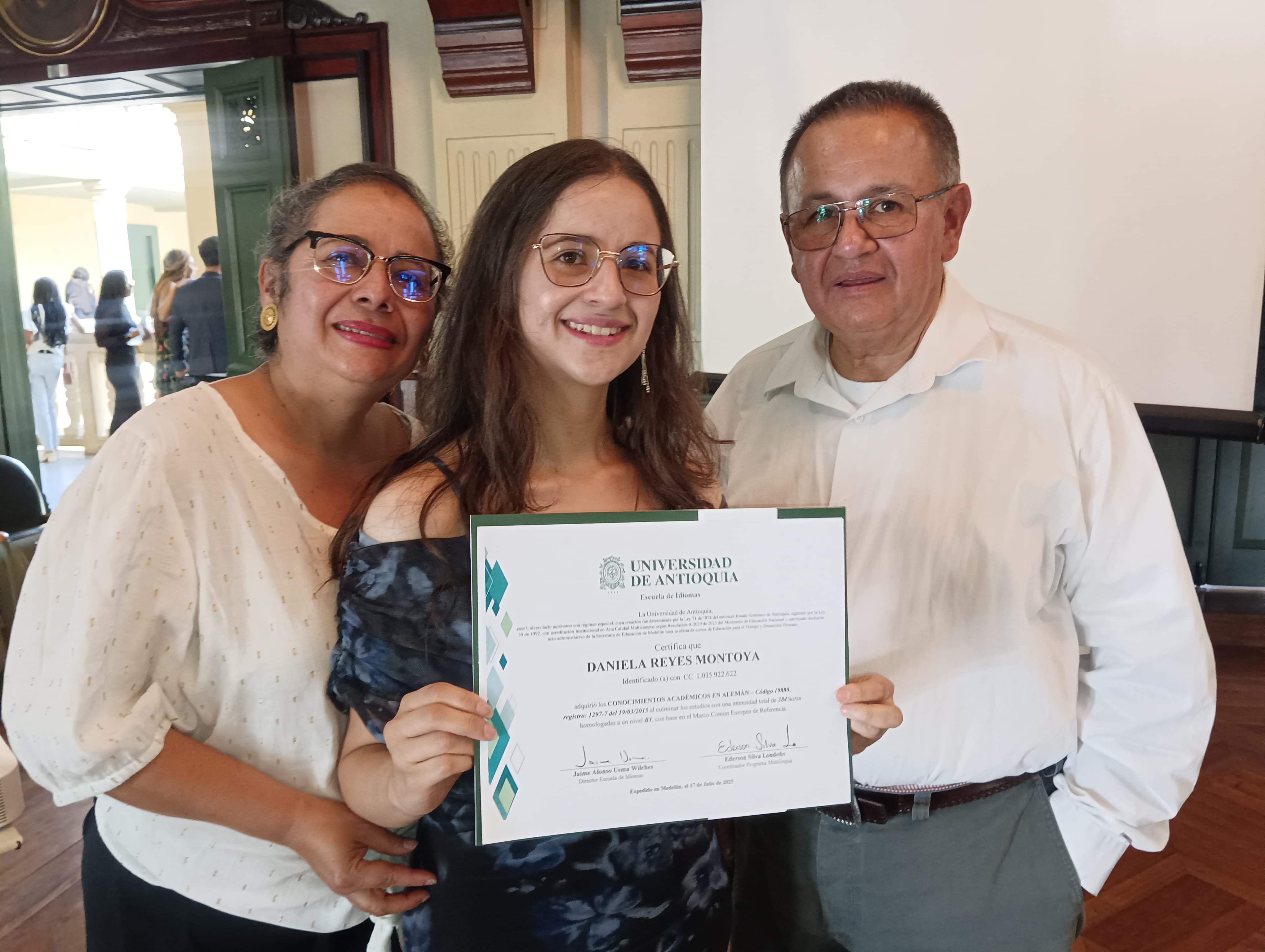 Tres personas de pie. La del medio con diploma en las manos