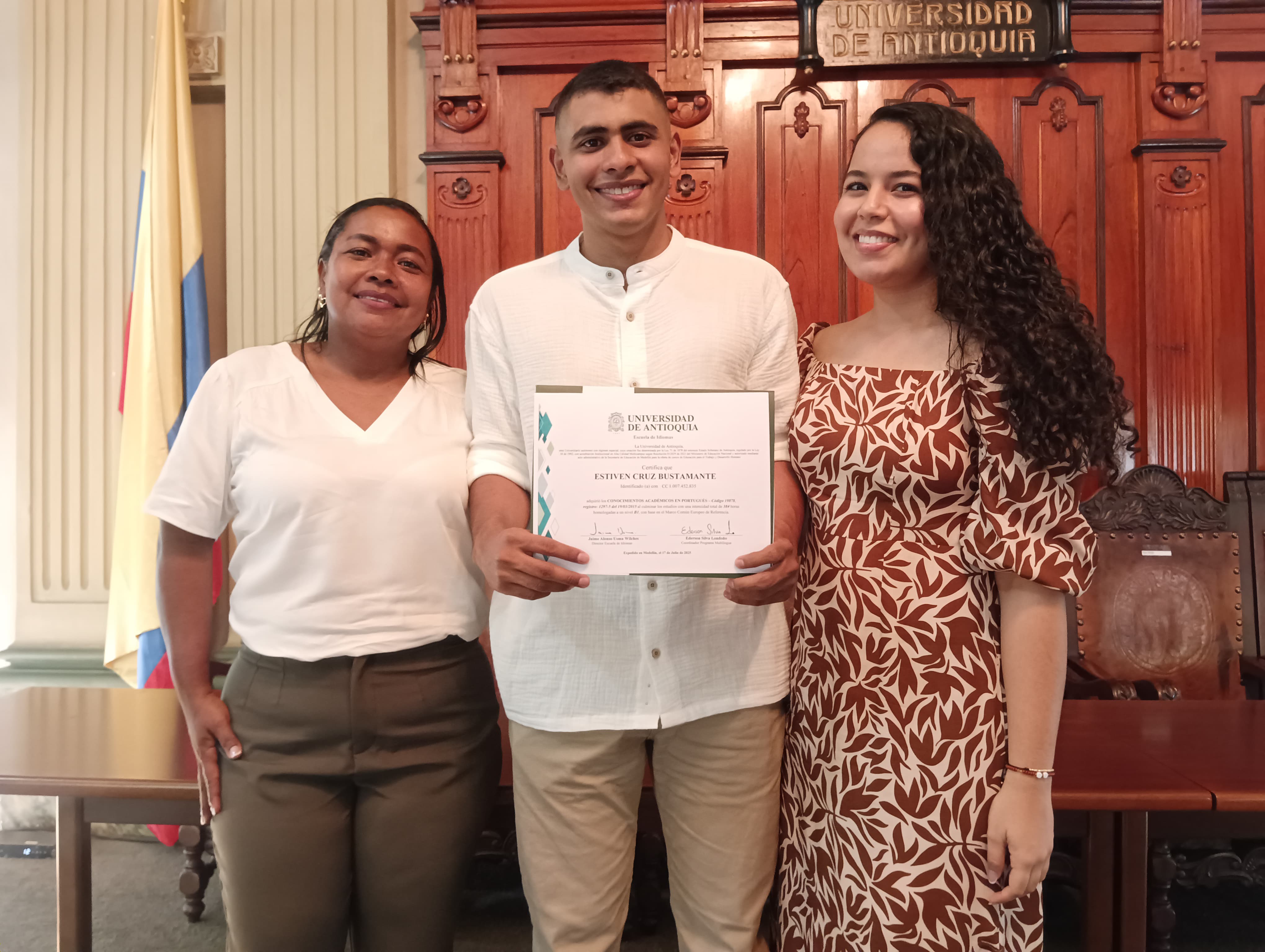 Tres personas de pie. La del medio con diploma en las manos