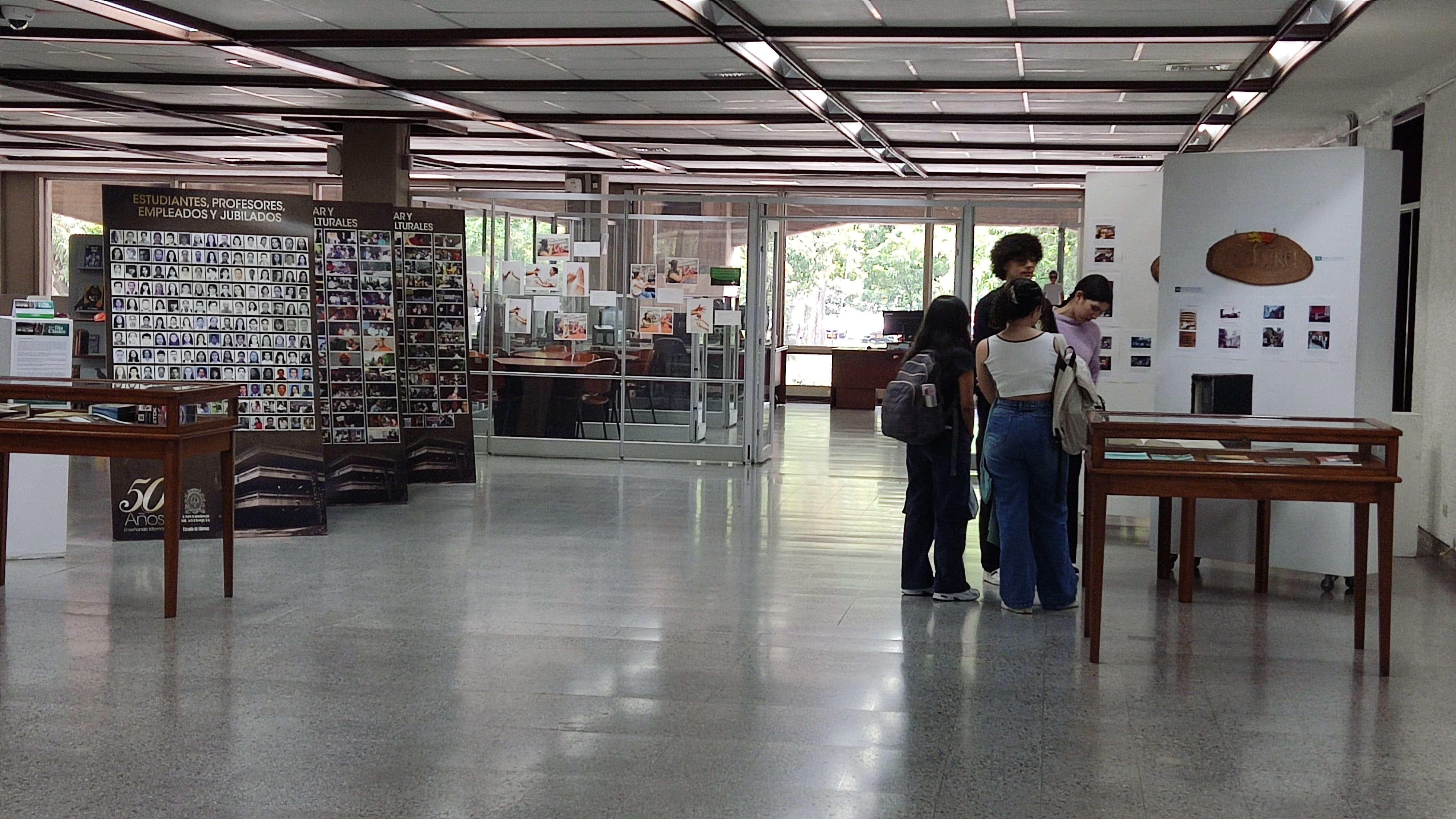 Estudiantes de pie en la biblioteca. Exposición 64 años de la Escuela de Idiomas