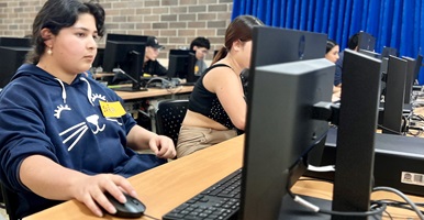 Una estudiante frente a un computador con su mano derecha sobre el mouse