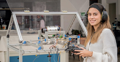 Estudiante del campus El Carmen de Viboral en el Laboratorio de Mecatrónica. Sostiene un control remoto y mira a la cámara.