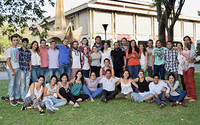 33 estudiantes de mɨnɨka posando al lado de la fuente de la udea abrazados, compartiendo alimentos y una bebé cargada por su padre.