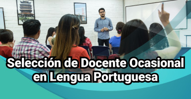 Estudiantes en salón de clase, uno de ellos levantando la mano, al fondo un docente