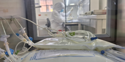 fotografía de medicamenteos almacenados en bolsas, de fondo se ve una persona trabajando en un laboratorio. Usa guantes, tapabocas y bata